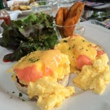 Los huevos Benedicto con el top del salmón ahumado con las hierbas y la salsa frescas del hollandaise sirven con la ensalada verd imagen de archivo Los huevos Benedicto con el top del salmón ahumado con las hierbas y la salsa frescas del hollandaise sirven con la ensalada verd imagen de archivo