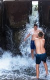 Los muchachos, adolescentes están jugando debajo de la cascada, en el río Mojado y feliz Imagen de archivo libre de regalías Los muchachos, adolescentes están jugando debajo de la cascada, en el río Mojado y feliz Imagen de archivo libre de regalías