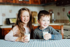 Los niños beben la leche y se divierten en la cocina en la mañana Hermana y hermano que sostienen vidrios llenos de leche imagen de archivo Los niños beben la leche y se divierten en la cocina en la mañana Hermana y hermano que sostienen vidrios llenos de leche imagen de archivo
