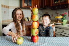 Los niños comen manzanas y se divierten en la cocina en la mañana imágenes de archivo libres de regalías Los niños comen manzanas y se divierten en la cocina en la mañana imágenes de archivo libres de regalías