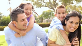 Los padres que dan a niños llevan a cuestas paseo en parque almacen de video Los padres que dan a niños llevan a cuestas paseo en parque almacen de video