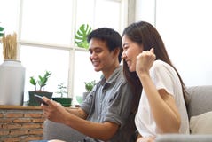 Los pares jovenes que se sientan en el sofá están mirando el teléfono móvil y están sintiendo surprise&happy cuando conozca el re foto de archivo libre de regalías Los pares jovenes que se sientan en el sofá están mirando el teléfono móvil y están sintiendo surprise&happy cuando conozca el re foto de archivo libre de regalías