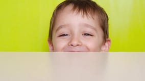 Los pequeños juegos de niños, ocultando debajo de la tabla Un muchacho de risa feliz aparece de debajo la tabla y mira en metrajes Los pequeños juegos de niños, ocultando debajo de la tabla Un muchacho de risa feliz aparece de debajo la tabla y mira en metrajes
