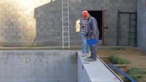 Los trabajadores constructivos en un casco discuten casas del edificio de la construcción con una piscina metrajes Los trabajadores constructivos en un casco discuten casas del edificio de la construcción con una piscina metrajes