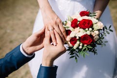 Love and marriage. Fine art rustic wedding ceremony outside. Groom putting golden ring on the bride`s finger. Bouquet of red and