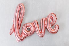 Love word from pink inflatable balloon on grey concrete background. The concept of romance, Valentine`s Day. Love rose gold foil