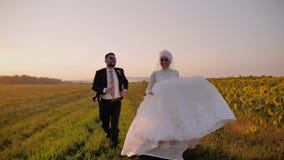 Lovers boy and girl running on a beautiful field of sunflowers. They both smile. The girl is wearing a beautiful white dress. stock video footage Lovers boy and girl running on a beautiful field of sunflowers. They both smile. The girl is wearing a beautiful white dress. stock video footage