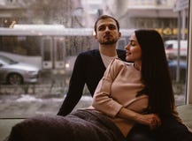Loving couple. Guy and his girlfriend dressed in in sweaters and jeans sitting close to each other on the windowsill in stock image Loving couple. Guy and his girlfriend dressed in in sweaters and jeans sitting close to each other on the windowsill in stock image