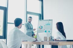Low angle shot of a young smart brunet bearded manager in spectacles, reporting to the team of colleagues with the flip chart. royalty free stock photography Low angle shot of a young smart brunet bearded manager in spectacles, reporting to the team of colleagues with the flip chart. royalty free stock photography