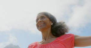 Low angle view of active senior African American woman stretching her arms in sunshine on the beach stock footage Low angle view of active senior African American woman stretching her arms in sunshine on the beach stock footage