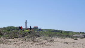 Ludzie chodzi wzdłuż plażowej ścieżki blisko morza z latarnią morską na tle w Paphos, Cypr zbiory Ludzie chodzi wzdłuż plażowej ścieżki blisko morza z latarnią morską na tle w Paphos, Cypr zbiory