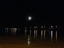 Luna que enarbola hacia fuera de detrás las nubes que reflejan sobre el agua fotografía de archivo Luna que enarbola hacia fuera de detrás las nubes que reflejan sobre el agua fotografía de archivo
