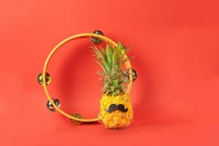 Lustige zurechtgemachte Ananas mit schwarzem Schnurrbarttamburin-Korallenhintergrund Das Konzept des Entspannung und der musikali lizenzfreie stockfotos Lustige zurechtgemachte Ananas mit schwarzem Schnurrbarttamburin-Korallenhintergrund Das Konzept des Entspannung und der musikali lizenzfreie stockfotos