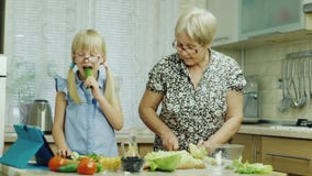 Lustiges Mädchen 6 Jahre alte Hilfen ihre Großmutter bereiten Mahlzeiten in der Küche vor Isst eine Gurke, hat Spaß zusammen Gesu stock video Lustiges Mädchen 6 Jahre alte Hilfen ihre Großmutter bereiten Mahlzeiten in der Küche vor Isst eine Gurke, hat Spaß zusammen Gesu stock video
