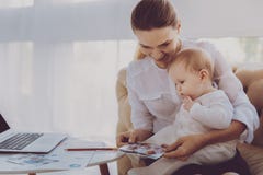 Lycklig familjkvinna som visar foto till hennes småbarn som sitter i vardagsrum royaltyfria bilder Lycklig familjkvinna som visar foto till hennes småbarn som sitter i vardagsrum royaltyfria bilder