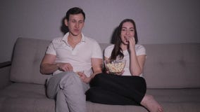 Lyckliga par som hemma håller ögonen på en film på tvsammanträde på en soffa stock video Lyckliga par som hemma håller ögonen på en film på tvsammanträde på en soffa stock video