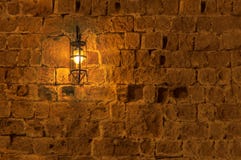 Lámpara ligera vieja en la ejecución de la noche en una pared medieval de la fortaleza de la calle Fotografía de archivo libre de regalías Lámpara ligera vieja en la ejecución de la noche en una pared medieval de la fortaleza de la calle Fotografía de archivo libre de regalías