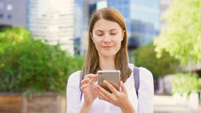Lächelnde Geschäftsfrau im weißen Hemd, das im im Stadtzentrum gelegenen Geschäftsgebiet unter Verwendung des Smartphone steht stock video Lächelnde Geschäftsfrau im weißen Hemd, das im im Stadtzentrum gelegenen Geschäftsgebiet unter Verwendung des Smartphone steht stock video