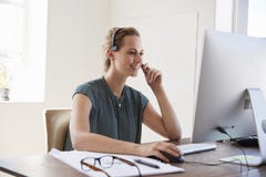 Lächelnde weiße Frau am Computer in einem tragenden Kopfhörer des Büros stockbilder Lächelnde weiße Frau am Computer in einem tragenden Kopfhörer des Büros stockbilder