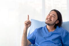 Lächelnder asiatischer Patient, der auf Krankenhausbett mit dem Finger oben zeigt sitzt lizenzfreie stockfotografie Lächelnder asiatischer Patient, der auf Krankenhausbett mit dem Finger oben zeigt sitzt lizenzfreie stockfotografie