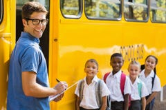 Lächelnder Lehrer, der Check-Liste von Kindern beim Hereinkommen in Bus aktualisiert stockfotografie Lächelnder Lehrer, der Check-Liste von Kindern beim Hereinkommen in Bus aktualisiert stockfotografie
