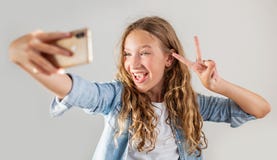 Lächelndes jugendlich Herstellungsselfie Foto auf Smartphone über nettem Mädchen des weißen Hintergrundes lizenzfreies stockbild Lächelndes jugendlich Herstellungsselfie Foto auf Smartphone über nettem Mädchen des weißen Hintergrundes lizenzfreies stockbild