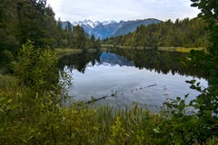 Löst naturlandskap med olik vegetation och den fridsamma sjön av ursprungligt klart vatten med bergspegelreflexion, Nya Zeeland arkivfoto Löst naturlandskap med olik vegetation och den fridsamma sjön av ursprungligt klart vatten med bergspegelreflexion, Nya Zeeland arkivfoto