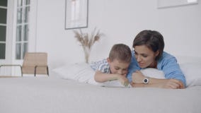 M?e nova feliz que mostra desenhos animados na tabuleta digital a seu filho da crian?a antes de ir dormir Exibição feliz da mãe vídeos de arquivo M?e nova feliz que mostra desenhos animados na tabuleta digital a seu filho da crian?a antes de ir dormir Exibição feliz da mãe vídeos de arquivo