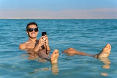 M?ody cz?owiek unosi si? na wodnej powierzchni nie?ywy morze i u?ywa jego smartphone fotografia stock M?ody cz?owiek unosi si? na wodnej powierzchni nie?ywy morze i u?ywa jego smartphone fotografia stock