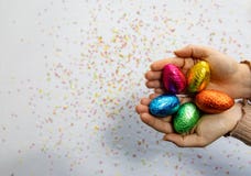 M?os da mulher que guardam ovos da p?scoa coloridos do chocolate com fundo branco e confetes borrados coloridos fotografia de stock M?os da mulher que guardam ovos da p?scoa coloridos do chocolate com fundo branco e confetes borrados coloridos fotografia de stock