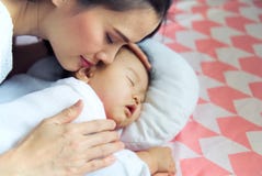 Madre asiática bonita joven que abraza a su bebé lindo durmiente en la cama La madre que se cierra los ojos al tocar a su niño su fotografía de archivo libre de regalías Madre asiática bonita joven que abraza a su bebé lindo durmiente en la cama La madre que se cierra los ojos al tocar a su niño su fotografía de archivo libre de regalías
