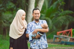 Madre di hijabi e passeggiata musulmane asiatiche del padre attraverso il parco con il figlio in passeggiatore mentre la sua mamm immagini stock Madre di hijabi e passeggiata musulmane asiatiche del padre attraverso il parco con il figlio in passeggiatore mentre la sua mamm immagini stock