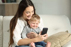 Madre e bambino che giocano con uno smartphone su uno strato immagine stock Madre e bambino che giocano con uno smartphone su uno strato immagine stock