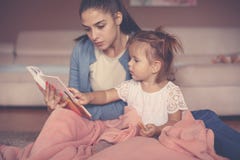 Madre e figlia a casa che si siedono sul pavimento e che leggono la BO fotografia stock libera da diritti Madre e figlia a casa che si siedono sul pavimento e che leggono la BO fotografia stock libera da diritti