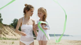 Madre e hija en el baile blanco de los bañadores con la cinta gimnástica en una playa arenosa Verano, amanecer almacen de metraje de vídeo Madre e hija en el baile blanco de los bañadores con la cinta gimnástica en una playa arenosa Verano, amanecer almacen de metraje de vídeo