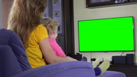 Madre feliz con su muchacha linda de la hija que mira historietas divertidas de la TV en el sofá Madre feliz con su muchacha linda de la hija que mira historietas divertidas de la TV en el sofá