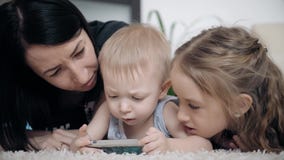 Madre joven y dos niños que se divierten con la tableta en el piso en casa, forma de vida almacen de metraje de vídeo Madre joven y dos niños que se divierten con la tableta en el piso en casa, forma de vida almacen de metraje de vídeo