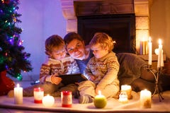 Madre joven y sus pequeños niños que se sientan por una chimenea en C Imagen de archivo libre de regalías Madre joven y sus pequeños niños que se sientan por una chimenea en C Imagen de archivo libre de regalías