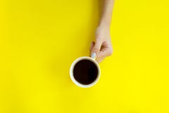 Main de femme tenant la tasse de café sur le fond jaune image stock Main de femme tenant la tasse de café sur le fond jaune image stock