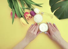 Mains femelles manucure, crème hydratante de crème, bien-être de produits de fleur de tulipe de mode de vie sur un fond jaune images stock Mains femelles manucure, crème hydratante de crème, bien-être de produits de fleur de tulipe de mode de vie sur un fond jaune images stock
