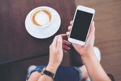 Mains tenant le téléphone portable blanc avec l'écran noir vide avec la tasse de café sur le fond en bois de table et de plancher Photo libre de droits Mains tenant le téléphone portable blanc avec l'écran noir vide avec la tasse de café sur le fond en bois de table et de plancher Photo libre de droits