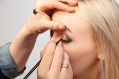The make-up artist with the help of a brush in one hand draws an arrow on the eyes of the girl, with the other hand pulls back the royalty free stock photos The make-up artist with the help of a brush in one hand draws an arrow on the eyes of the girl, with the other hand pulls back the royalty free stock photos