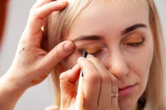 The make-up artist with the help of a pencil in one hand draws an arrow on the eyes of the model, with the other hand pulls back stock photography The make-up artist with the help of a pencil in one hand draws an arrow on the eyes of the model, with the other hand pulls back stock photography