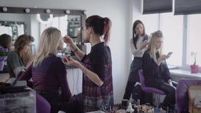 Make-upkünstler und Friseur des berühmten Kosmetiksalons arbeiten mit zwei Modellen, die für zukünftiges Schießen sich vorbereite stock video Make-upkünstler und Friseur des berühmten Kosmetiksalons arbeiten mit zwei Modellen, die für zukünftiges Schießen sich vorbereite stock video