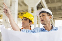 Male architect explaining building plan to colleague at construction site