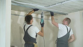 Male builders using electric drill assembling metal drywall profiles on construction site indoors