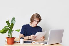 Male marketing expert reads attentively contract, studies charts and graphics, works with laptop computer at home, isolated over w stock photos Male marketing expert reads attentively contract, studies charts and graphics, works with laptop computer at home, isolated over w stock photos