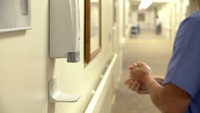 Male Nurse Using Hand Sanitizer In Hospital