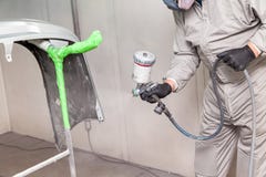 A male worker paints with a spray gun a part of the car body in silver after being damaged at an accident. Bumper from the vehicle stock photo A male worker paints with a spray gun a part of the car body in silver after being damaged at an accident. Bumper from the vehicle stock photo