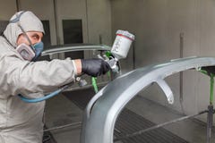 A male worker paints with a spray gun a part of the car body in silver after being damaged at an accident. Plastic elements from royalty free stock photography A male worker paints with a spray gun a part of the car body in silver after being damaged at an accident. Plastic elements from royalty free stock photography